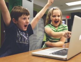 Zwei Kinder jubeln vor einem Laptop.