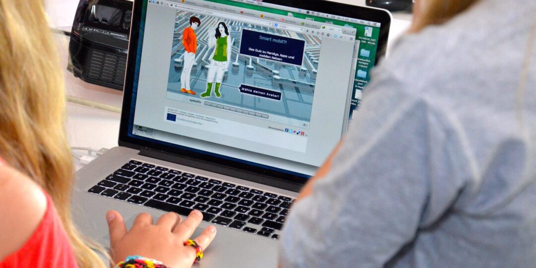 Zwei Menschen sitzen an einem Laptop.