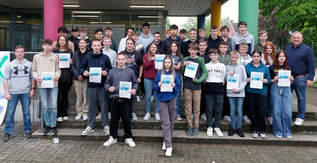 Schüler:innen der Emmy Noether Schule Neuenkirchen präsentieren ihre DiFü-Zertifikate. Daneben steht der verantwortliche Oberstudienrat Michael Leusmann.