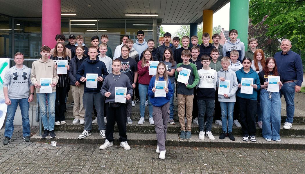 Schüler:innen der Emmy Noether Schule Neuenkirchen präsentieren ihre DiFü-Zertifikate. Daneben steht der verantwortliche Oberstudienrat Michael Leusmann.