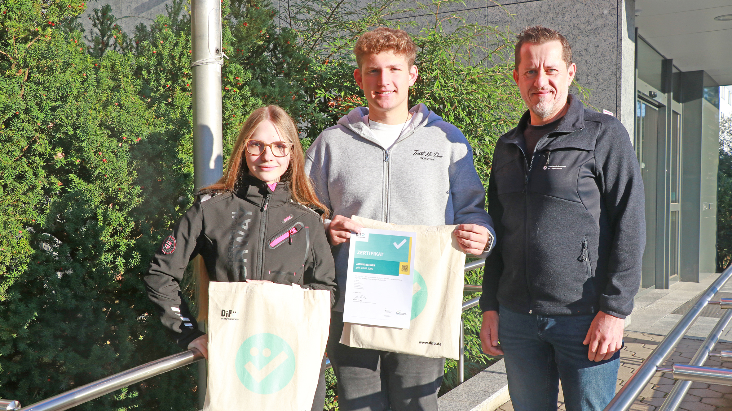 Zwei Azubis mit ihren DiFü-Zertifikaten neben Holger Bär, dem Beauftragten für Digitalisierung